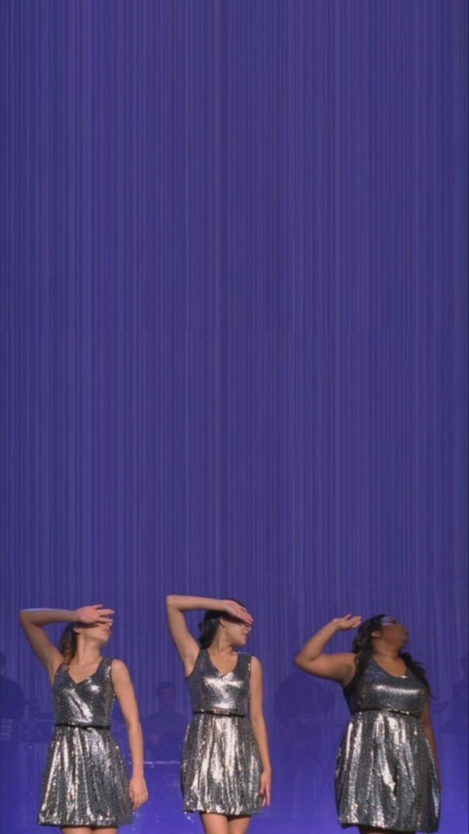 three women in silver dresses standing on stage with their hands behind their head and looking up at the sky