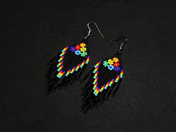 a pair of black earrings with multi colored beads on them, sitting on a black surface