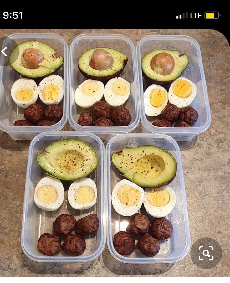 four plastic containers filled with eggs, meatballs and an avocado cut in half