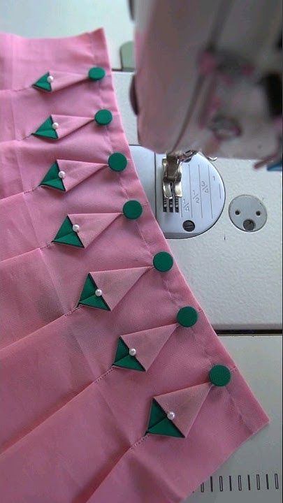 a sewing machine is working on a pink piece of fabric with green triangles and buttons