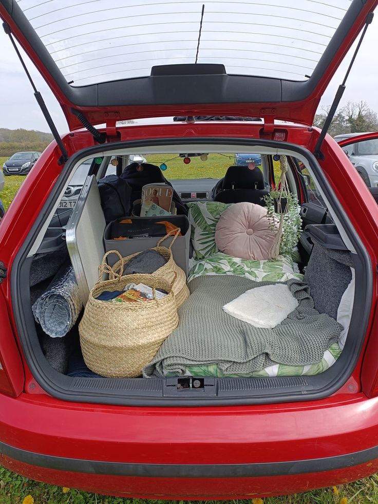 the trunk of a red car is filled with blankets, pillows and other things to put in it