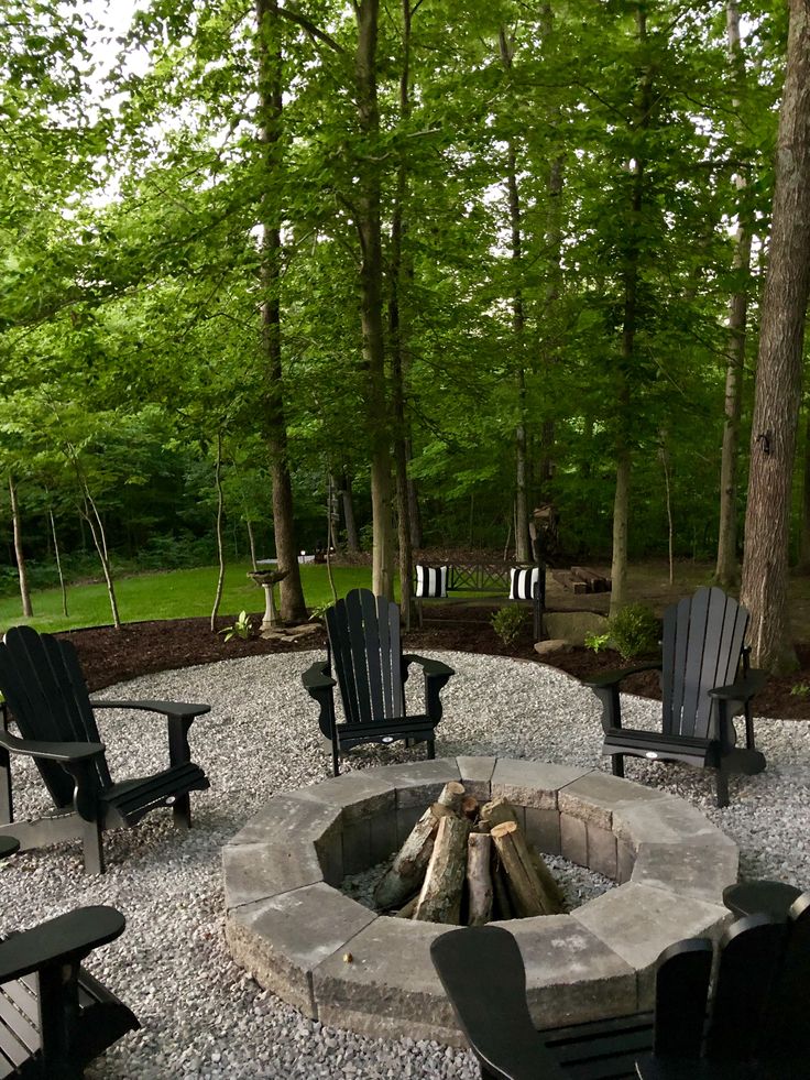 an outdoor fire pit surrounded by chairs and trees