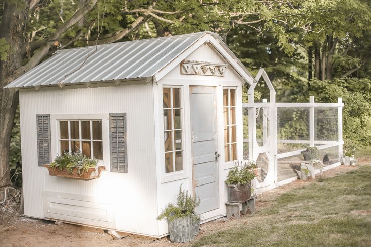 a small white shed sitting in the middle of a yard with potted plants on it