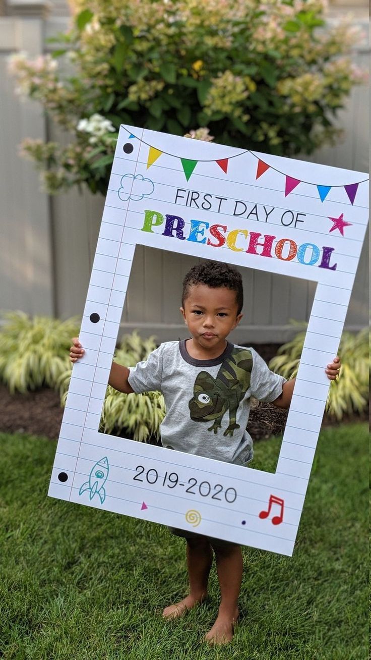 a young boy holding up a photo frame with the first day of preschool written on it