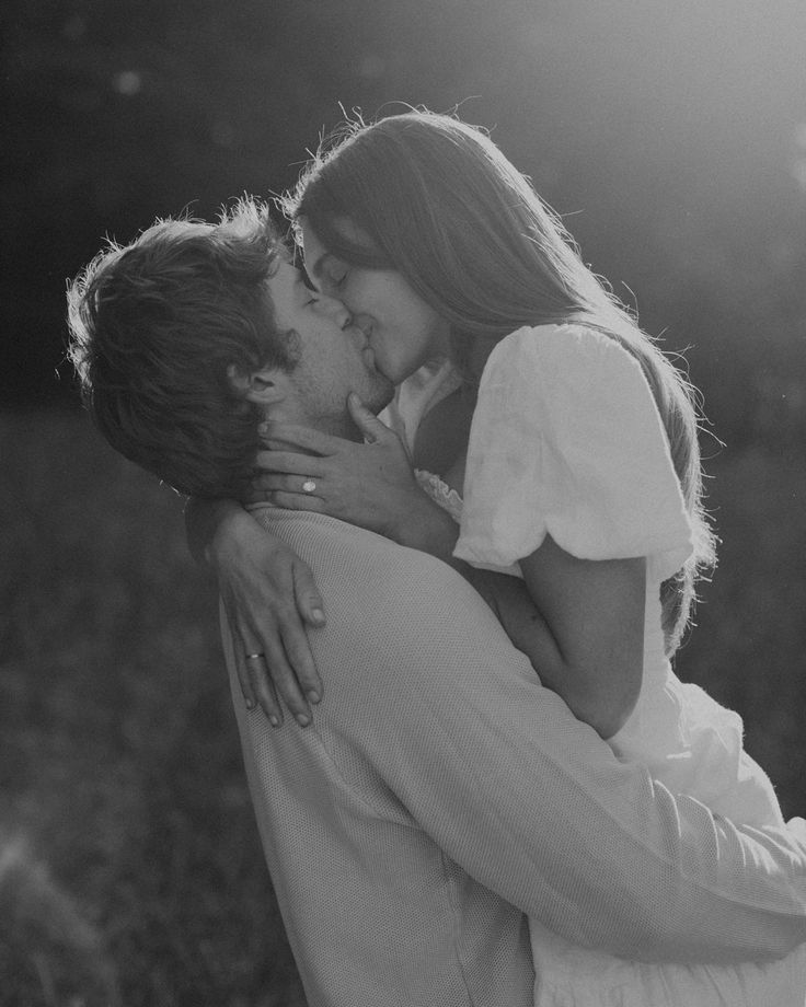 a man and woman kissing each other in black and white, with the sun shining on them