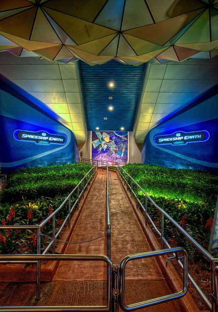 the inside of a building with stairs leading up to an entrance and green bushes on either side