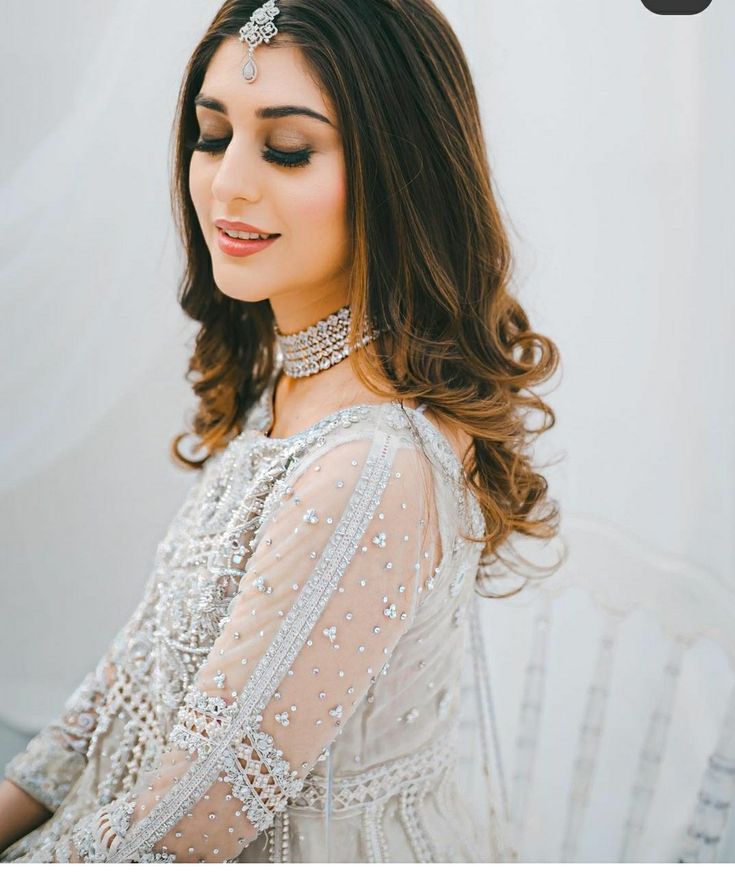 a woman with long hair wearing a white dress and headpiece in front of a wall