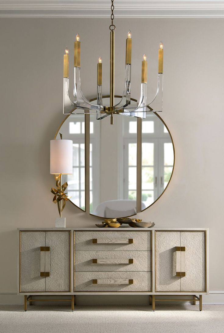 a large round mirror hanging on the wall above a dresser with four candles in it