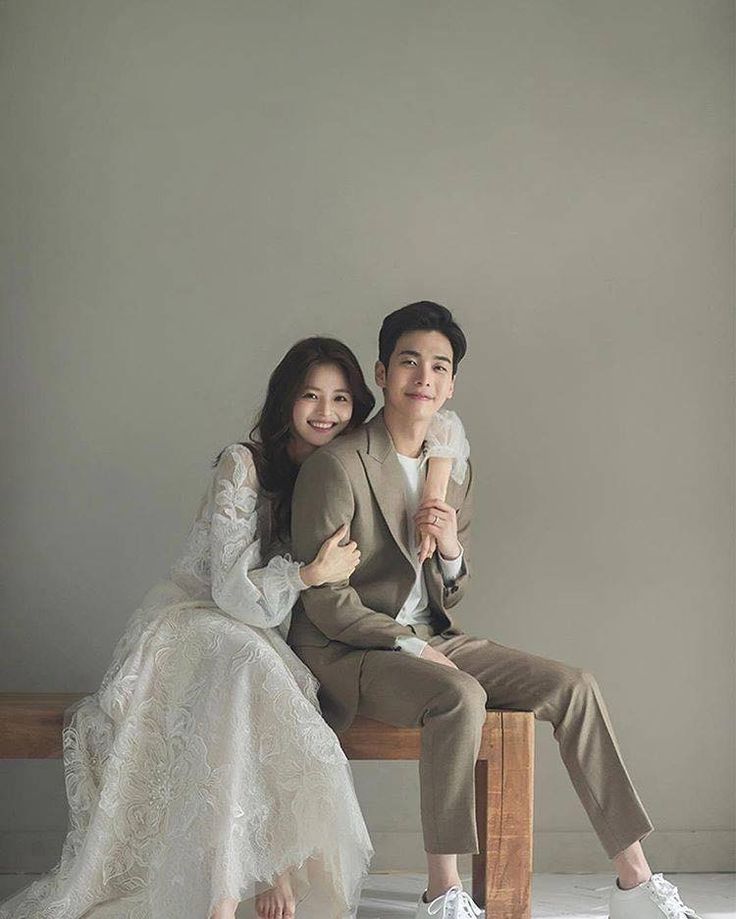 a man and woman are sitting on a bench posing for a wedding photo with their arms around each other