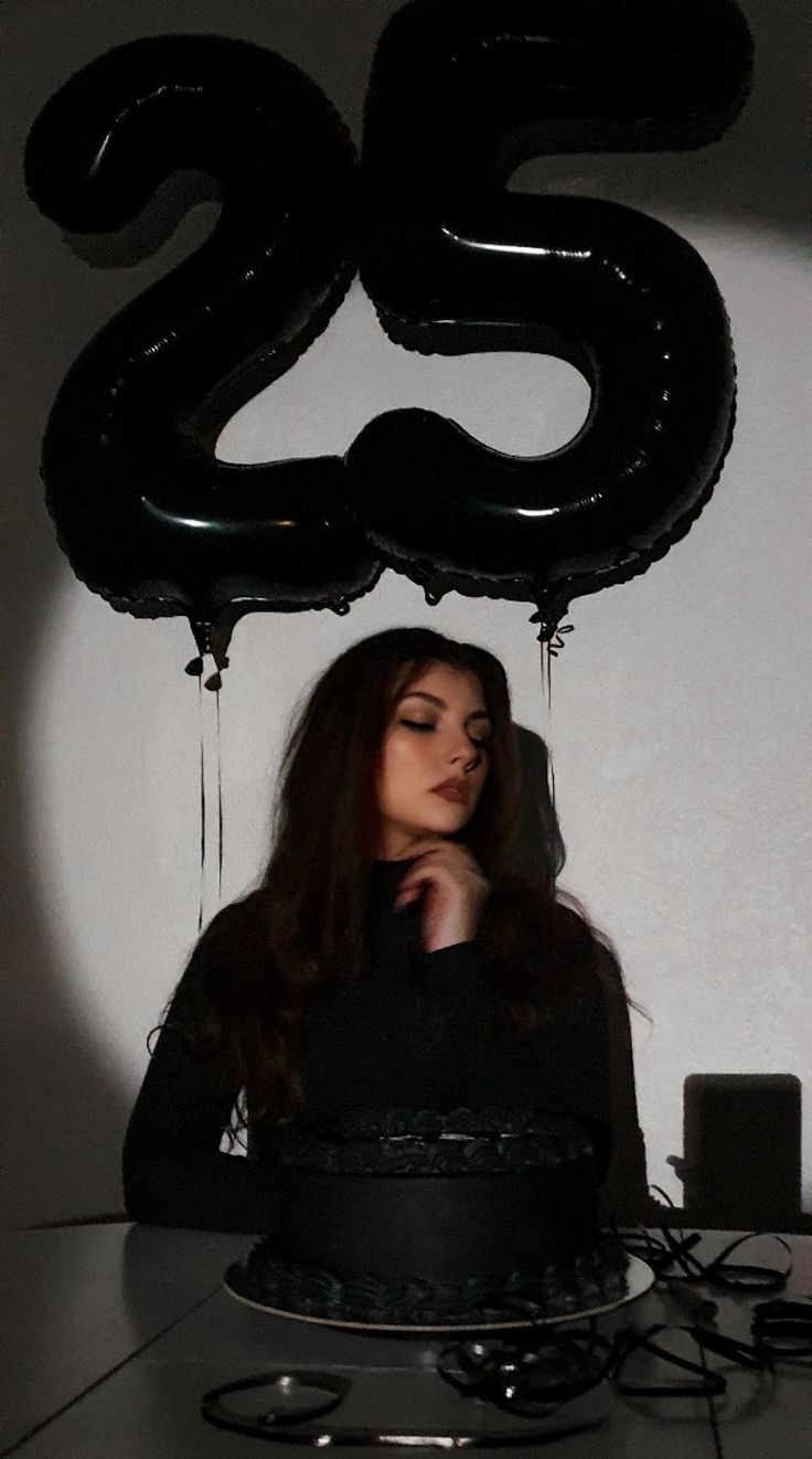 a woman sitting in front of a black cake with the number twenty five on it