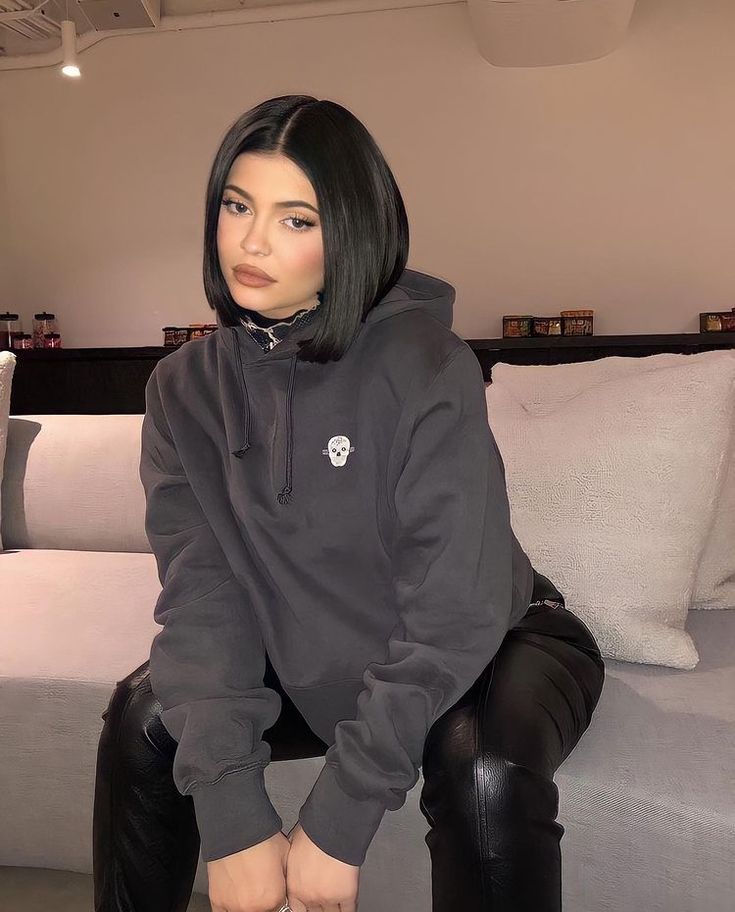 a woman sitting on top of a couch wearing black leather pants and a hoodie