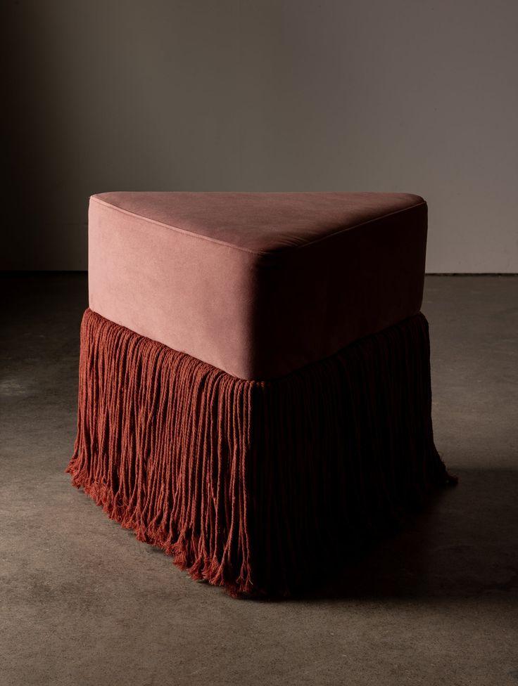 a pink ottoman with fringe on it in an empty room by the wall and floor