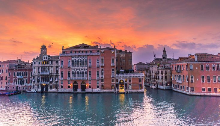 the sun is setting over some buildings on the water's edge in venice, italy