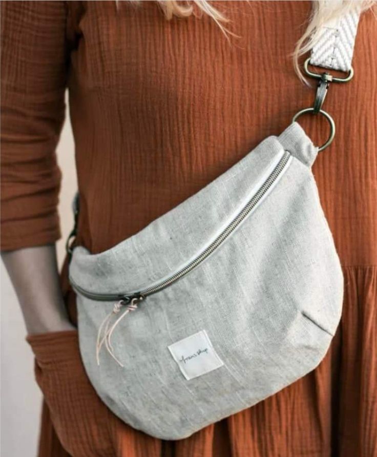 a woman wearing a gray fanny bag with a white tag on the front and silver zipper