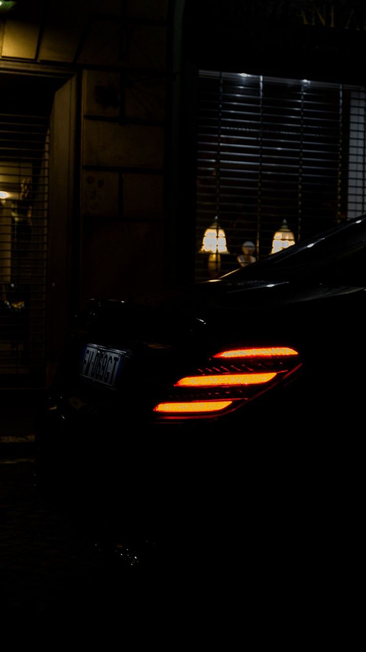 the back end of a car parked in front of a building at night with its lights on