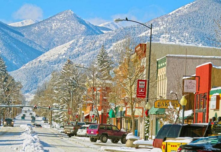 cars are parked on the street in front of snow - covered mountain tops and buildings