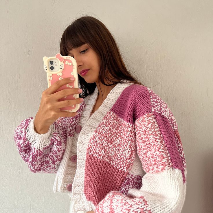 a woman taking a selfie with her cell phone while wearing a pink and white sweater