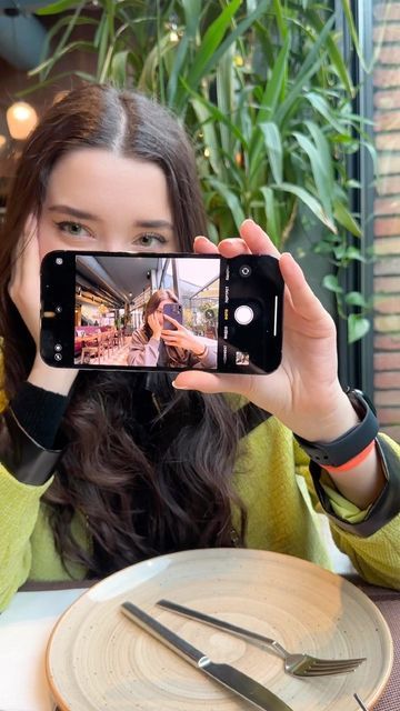 a woman taking a selfie with her cell phone at a table in a restaurant