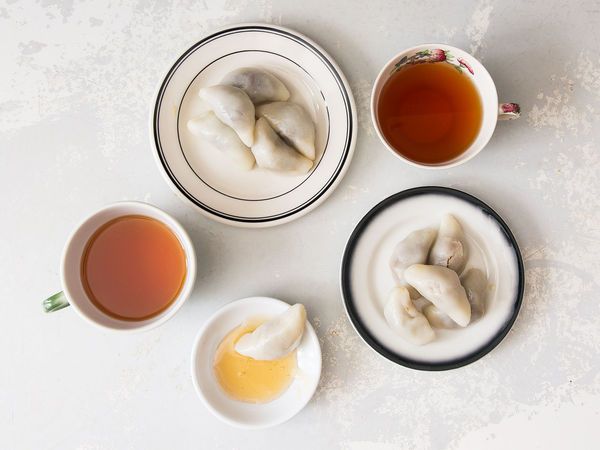 three bowls filled with dumplings next to two cups of tea