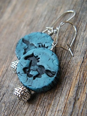 a pair of earrings that are on top of a wooden table and one is made out of clay