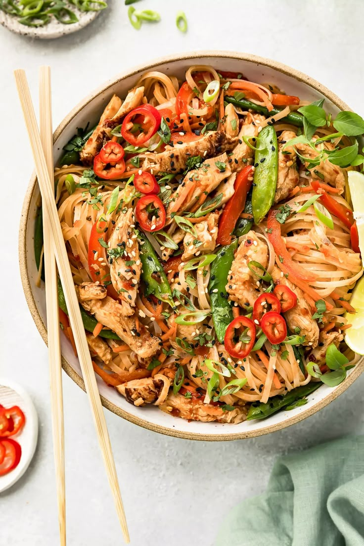 a bowl filled with noodles and vegetables next to chopsticks on a white surface