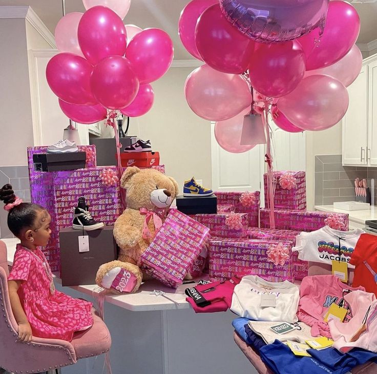 a room filled with lots of pink balloons and gifts on top of a table next to a teddy bear