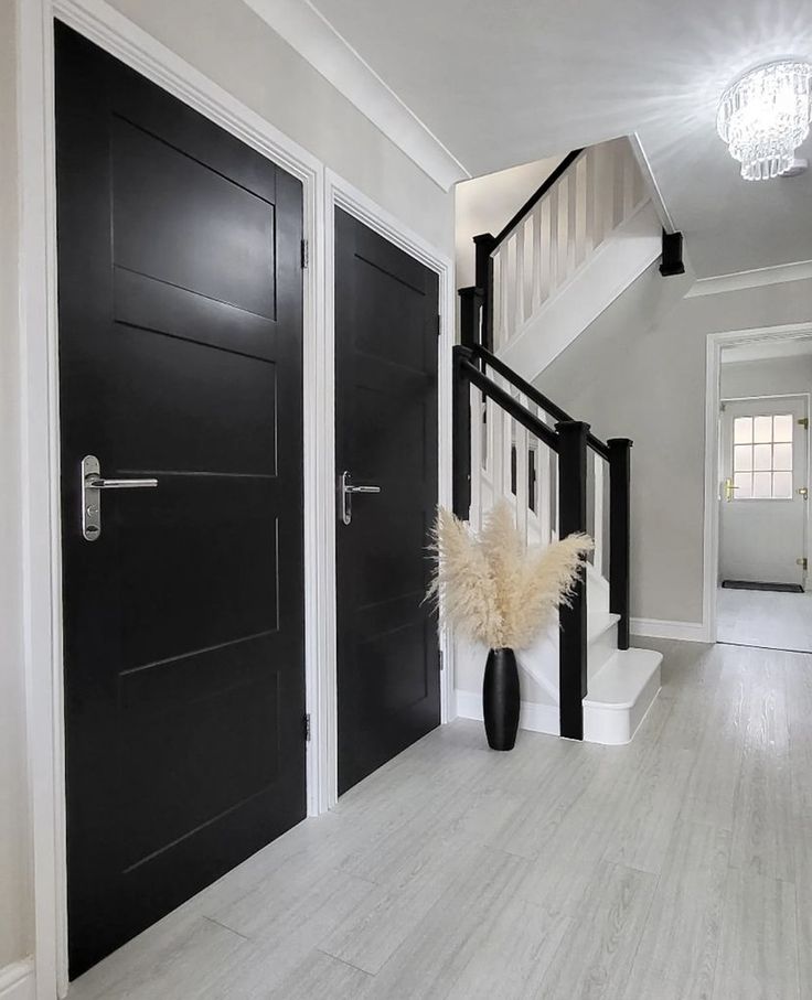 a black and white entryway with two large doors on each side, and a vase with dry grass in the foreground