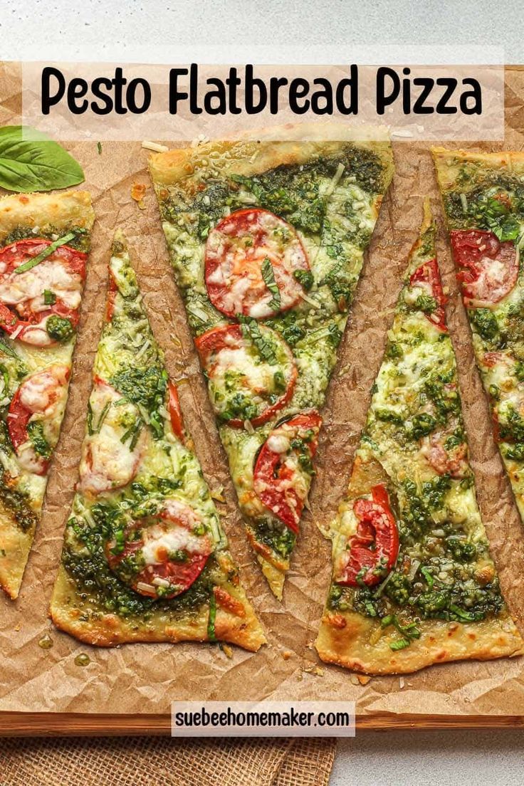 several slices of pesto flatbread pizza on a cutting board with basil and tomatoes