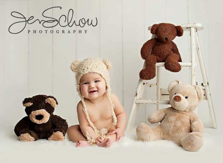 a baby sitting next to two teddy bears and one is smiling at the camera while wearing a hat