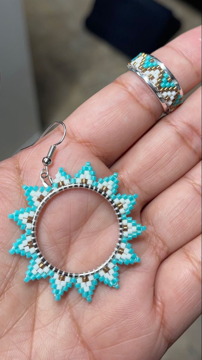 a hand holding a pair of earrings in it's left hand, with turquoise and brown beads