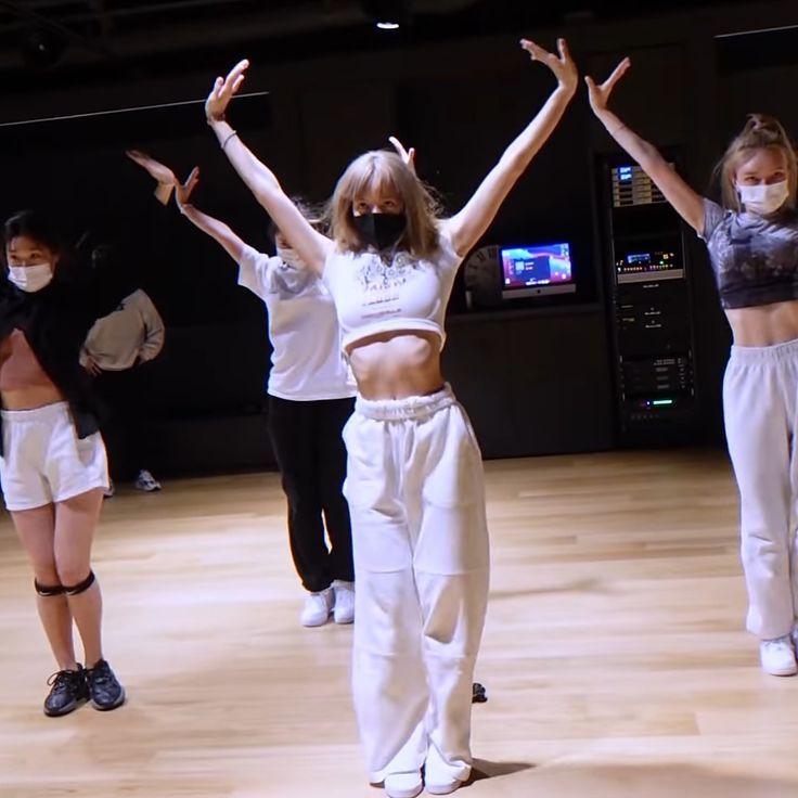 three girls in white pants and masks are standing on the floor with their hands up