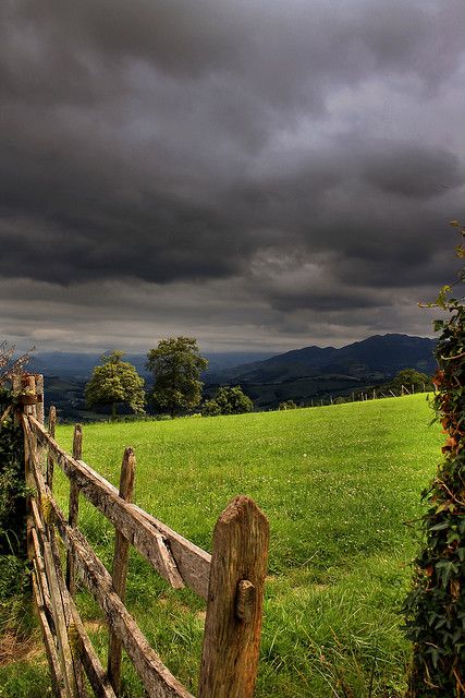 a wooden fence sitting in the middle of a lush green field under a cloudy sky