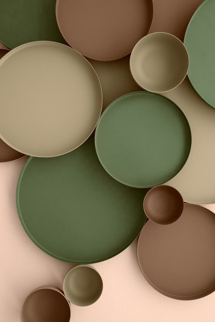 an array of plates and bowls are arranged on a pink surface with green, brown, and beige circles