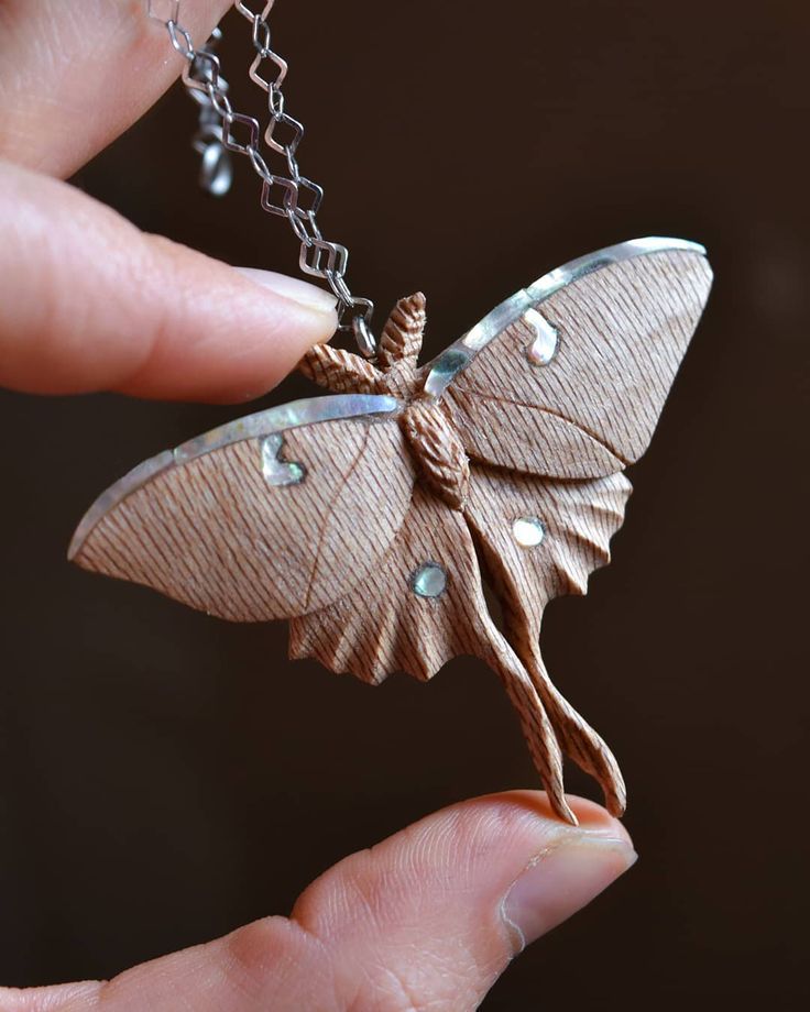 a hand holding a tiny butterfly necklace with pearls on it's wings and attached to a chain