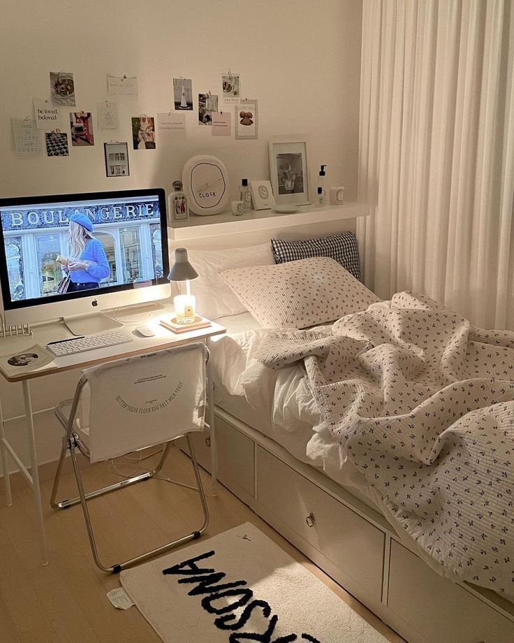 a bedroom with a bed, desk and computer monitor on the wall next to it