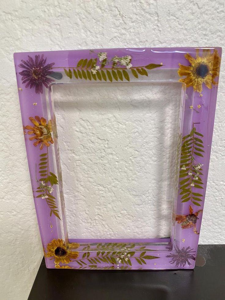 a purple frame with sunflowers and leaves painted on the sides, sitting on a table