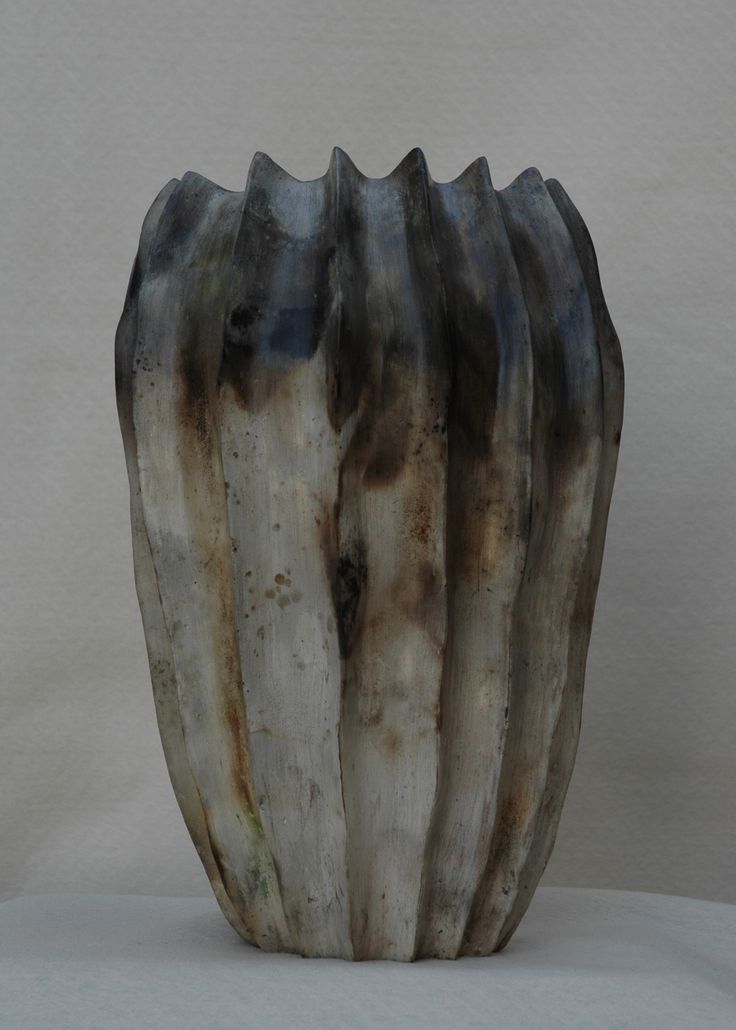 a vase made out of wood on a white tableclothed surface, with the top section partially covered in brown and black paint