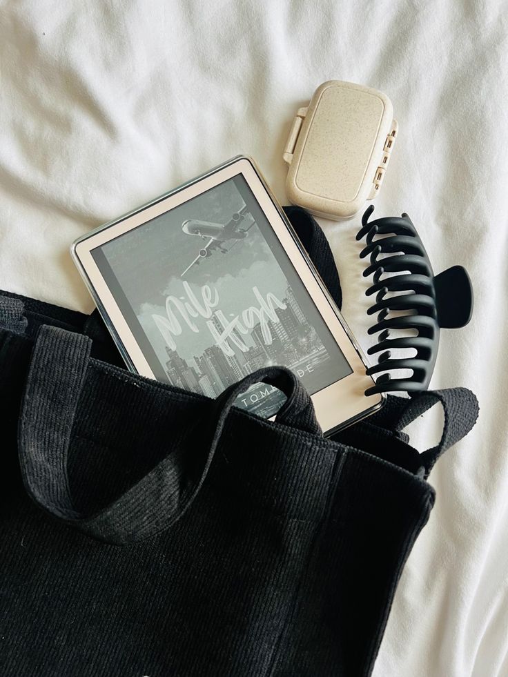 an electronic device sitting on top of a black bag next to a book and headphones