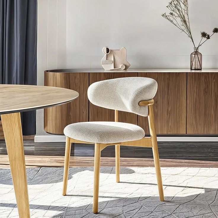 a white chair sitting next to a wooden table in a room with a vase on top of it