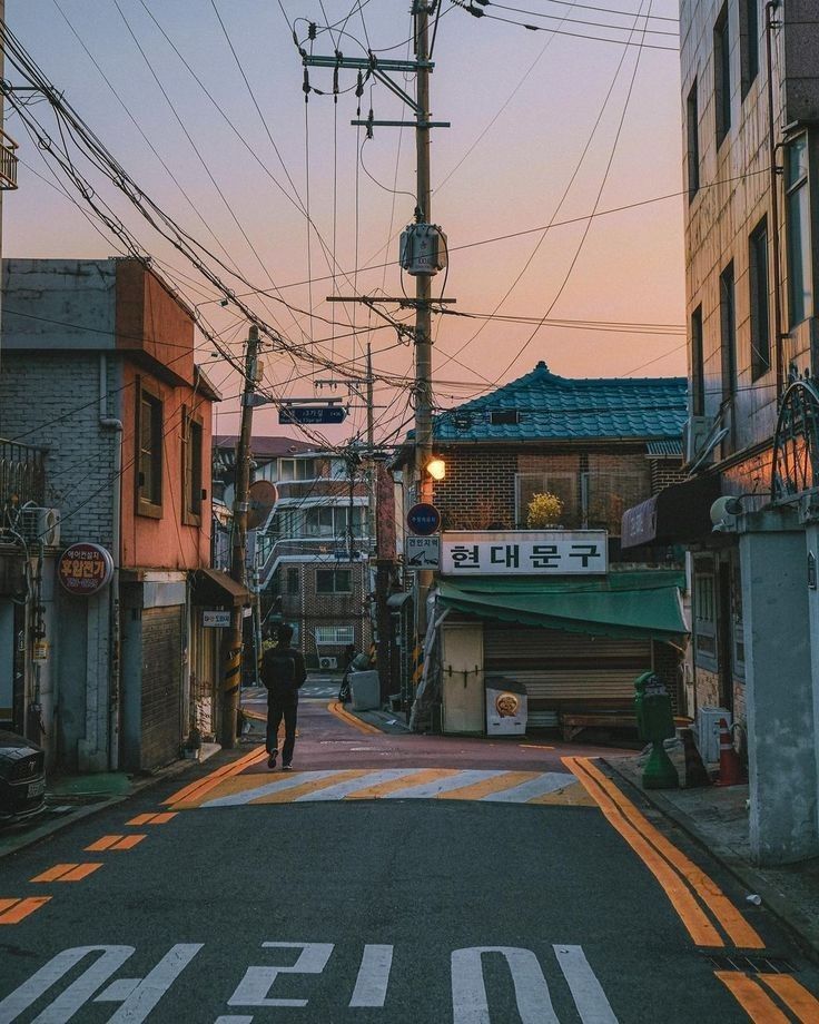 a person walking down an alley way in the middle of town with power lines overhead