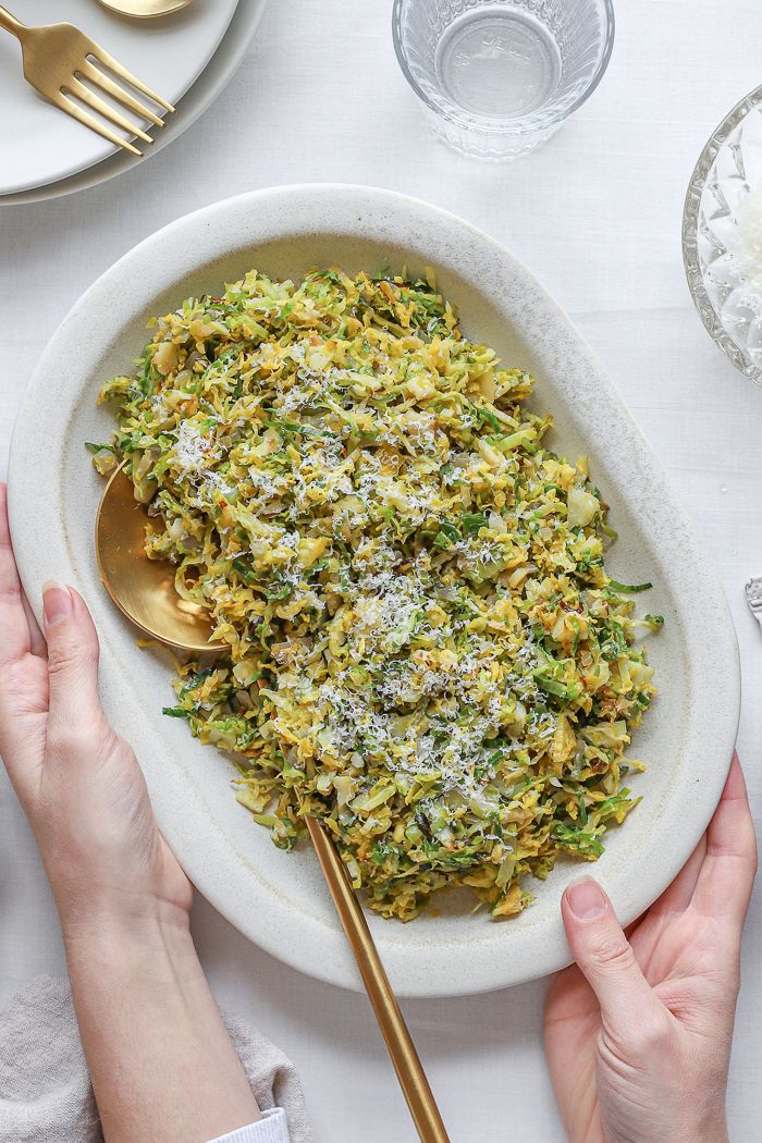 two hands holding a spoon over a bowl of food with broccoli and parmesan cheese