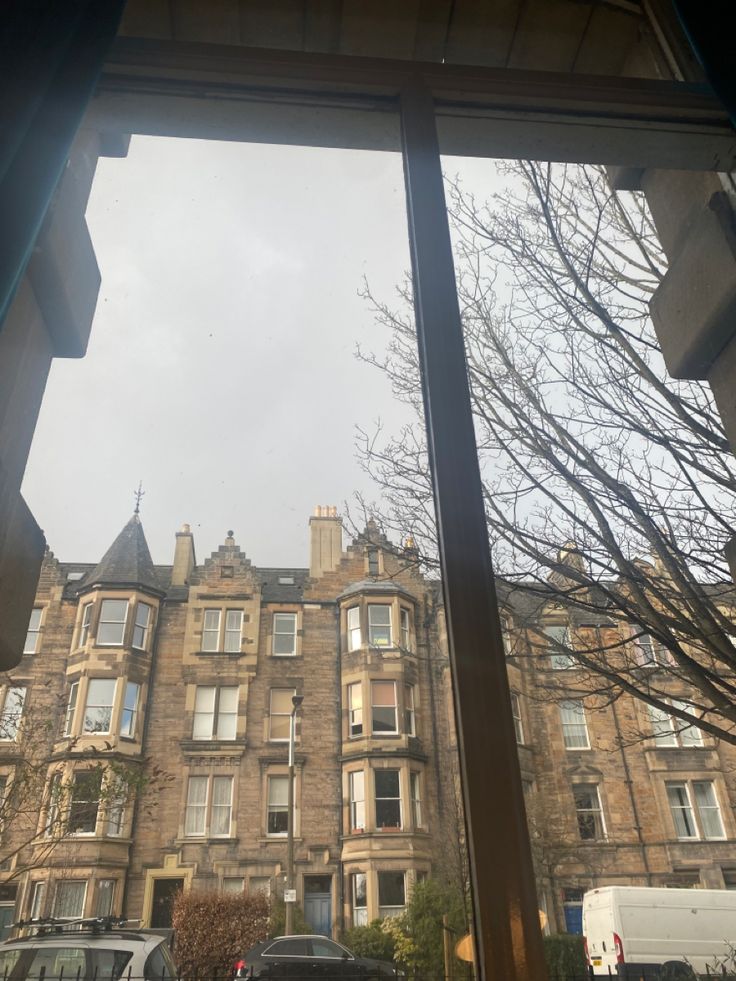 a large building seen through a window with cars parked on the street in front of it