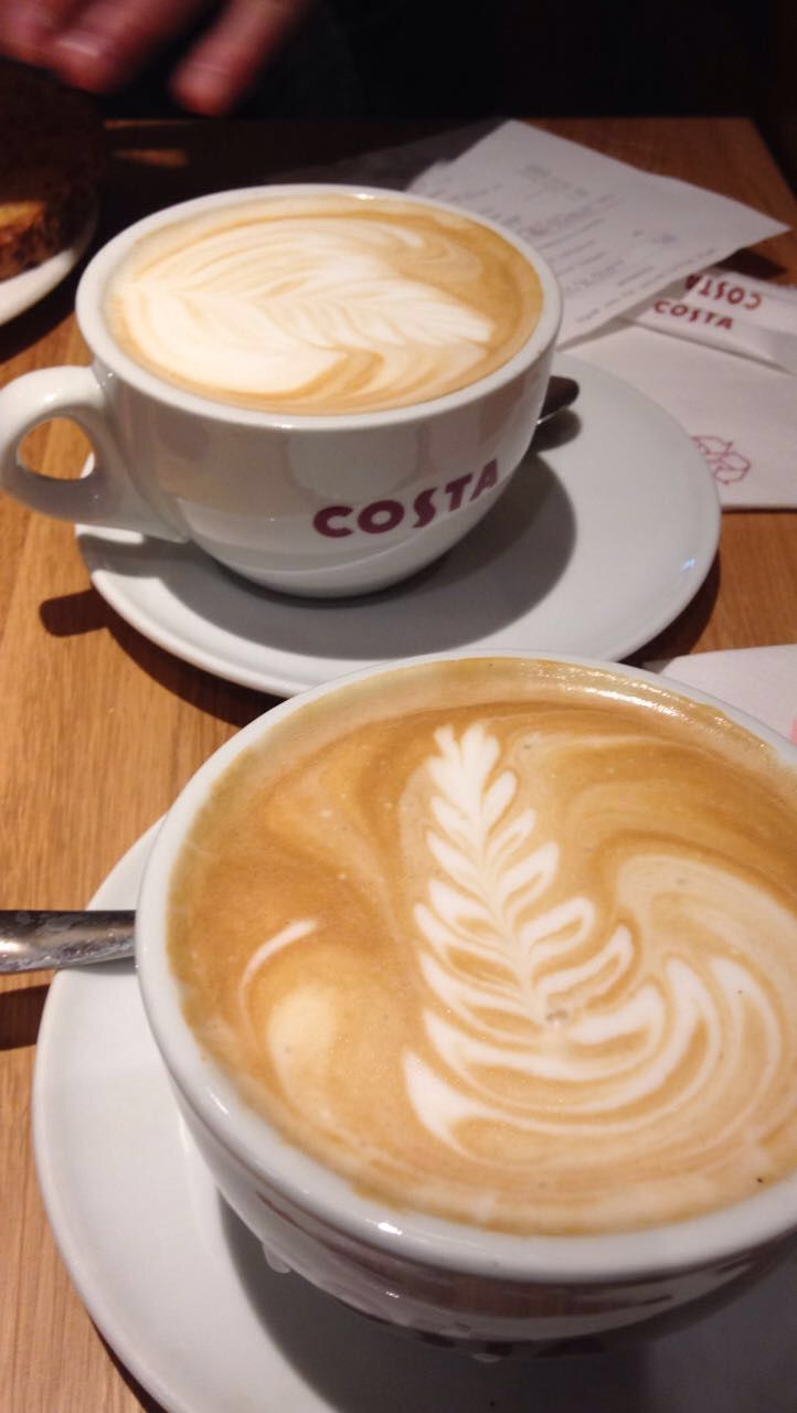 two cups of cappuccino sitting on top of white saucers next to each other