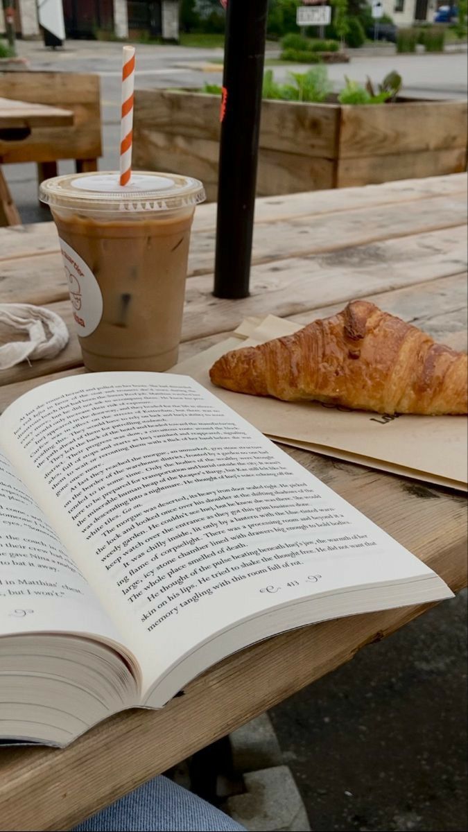 an open book sitting on top of a wooden table next to a cup of coffee