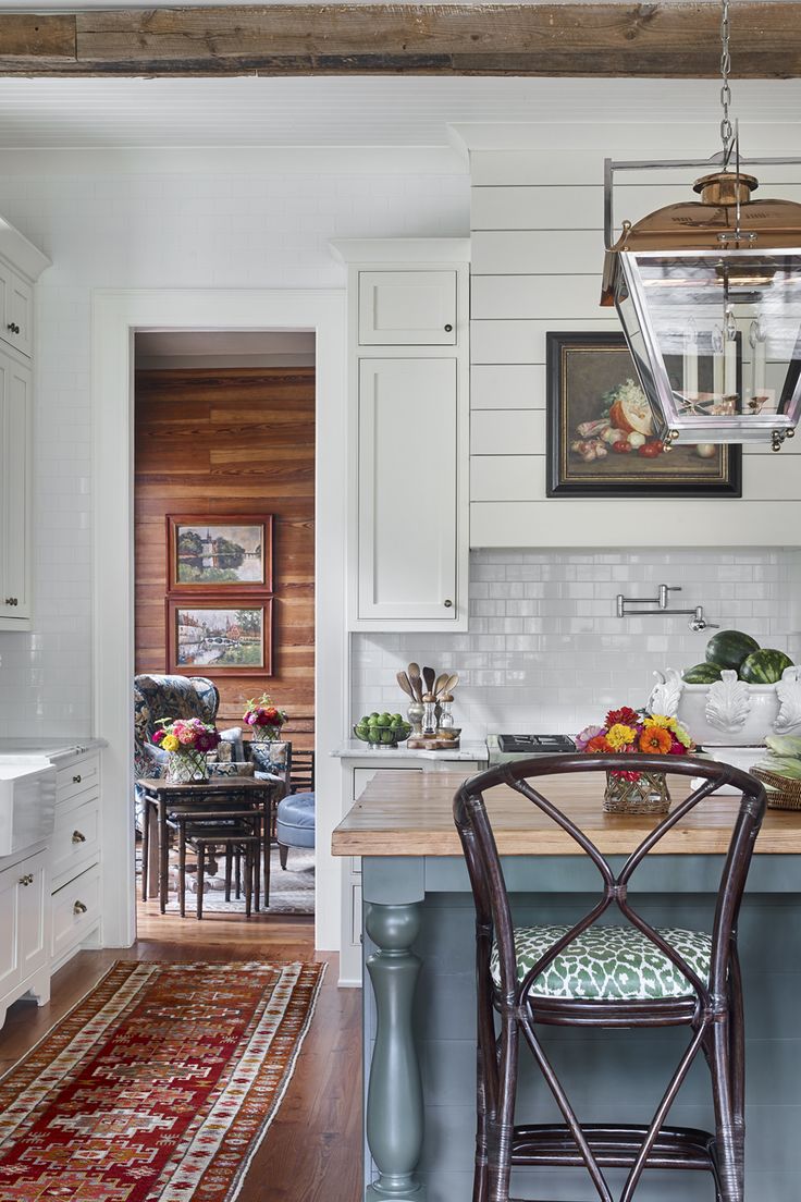 a kitchen with white cabinets and wooden flooring has an island in the middle that is surrounded by chairs