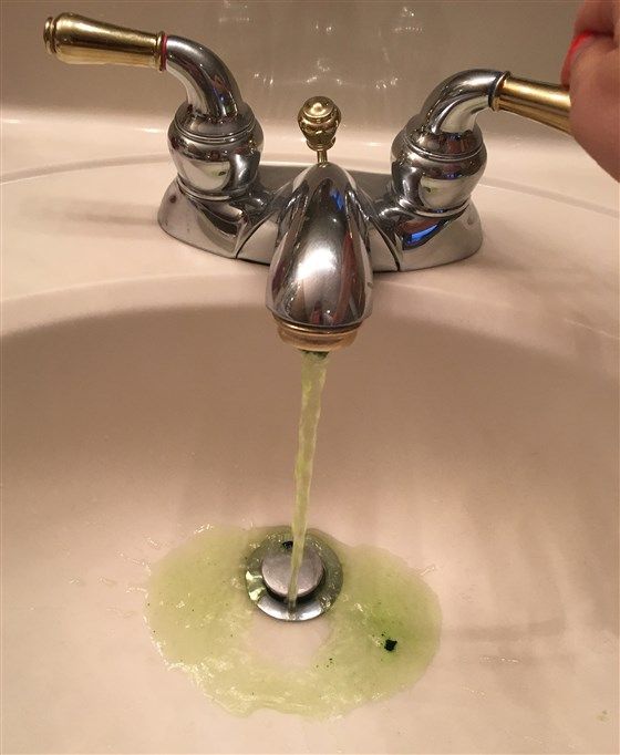 a person is pouring water from a faucet into a sink with green liquid