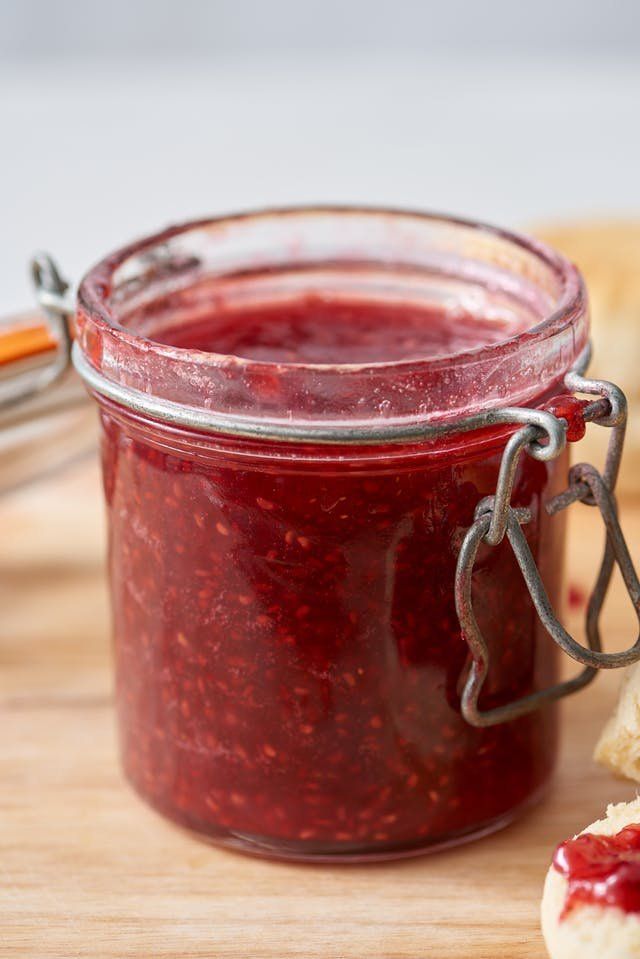 a jar of jam sitting on top of a wooden cutting board next to a cookie