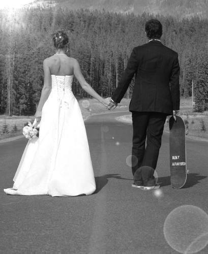 a bride and groom holding hands while walking down the road with their skateboard behind them