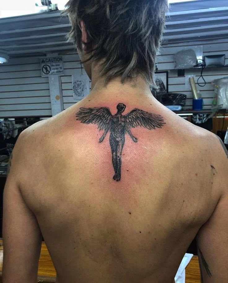 a man with a tattoo on his back is looking at the camera and he has an angel