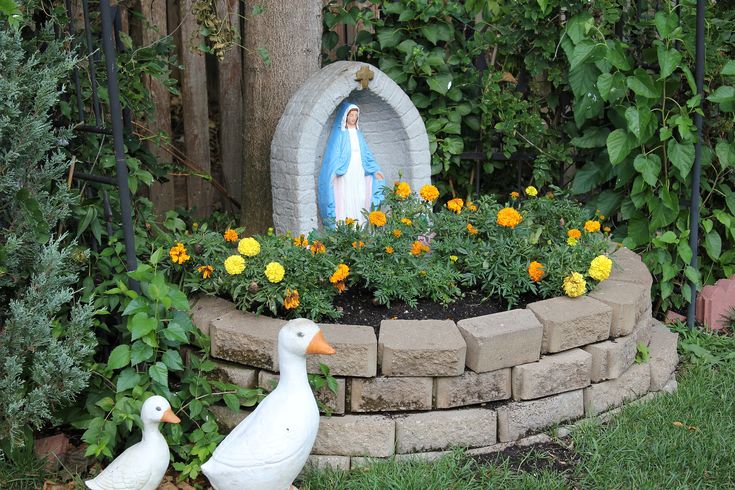 two white ducks walking around a garden with yellow flowers and a statue in the background